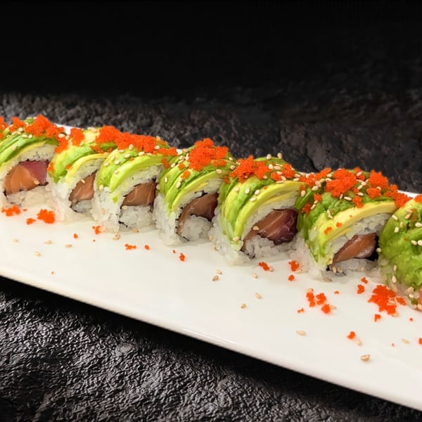 Dragon roll sushi with avocado, salmon, tuna, and orange tobiko on a white plate.