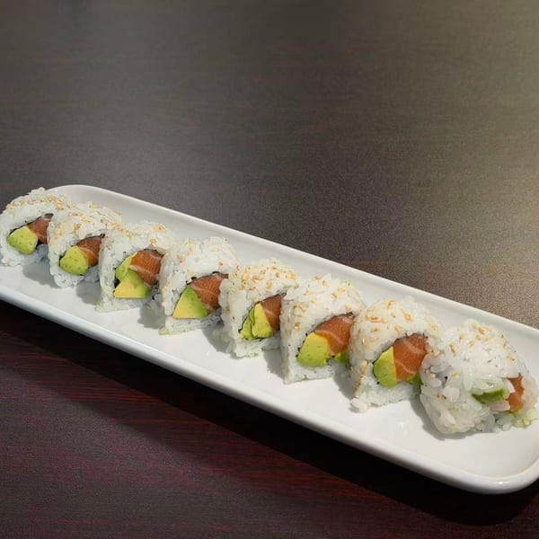 Seven pieces of salmon and avocado sushi rolls with sesame seeds on a white rectangular plate.