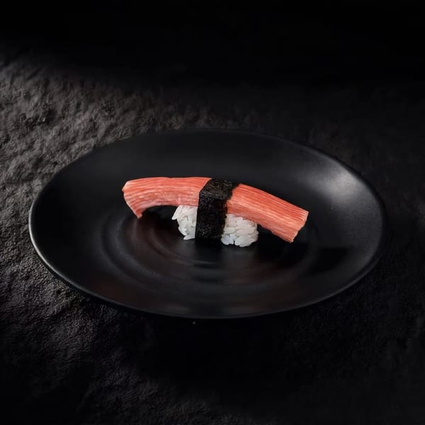 Single crab stick nigiri sushi on a black plate against a dark, textured background.