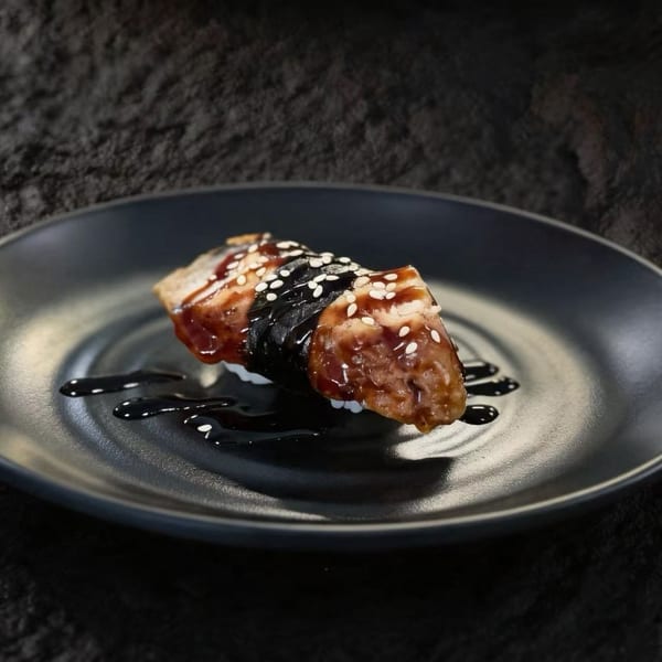 Unagi nigiri sushi with dark sauce and sesame seeds on a black plate.