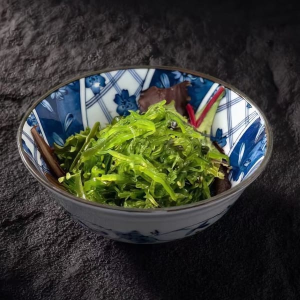 Bright green seaweed salad in a decorative blue and white bowl on a dark, textured surface.