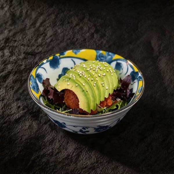 A colorful bowl of tuna tartare topped with sliced avocado and sesame seeds on a dark background.